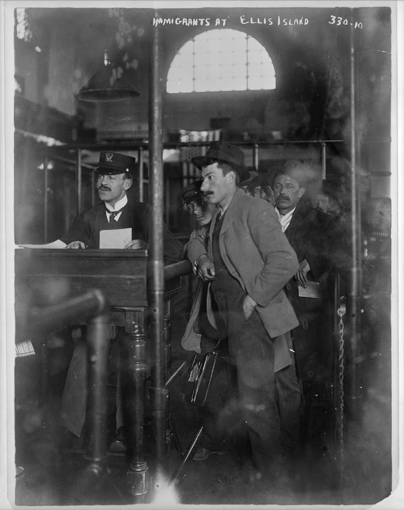 An immigrant standing before an inspector at a registration desk at Ellis Island, circa 1907 to 1917.